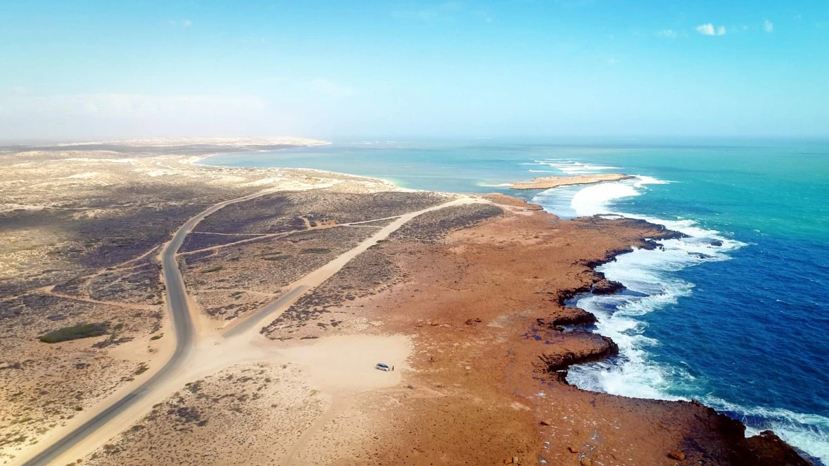 Bird's eye view of typical Australian scenery: ocean to the right, a road and desert landscape on the left