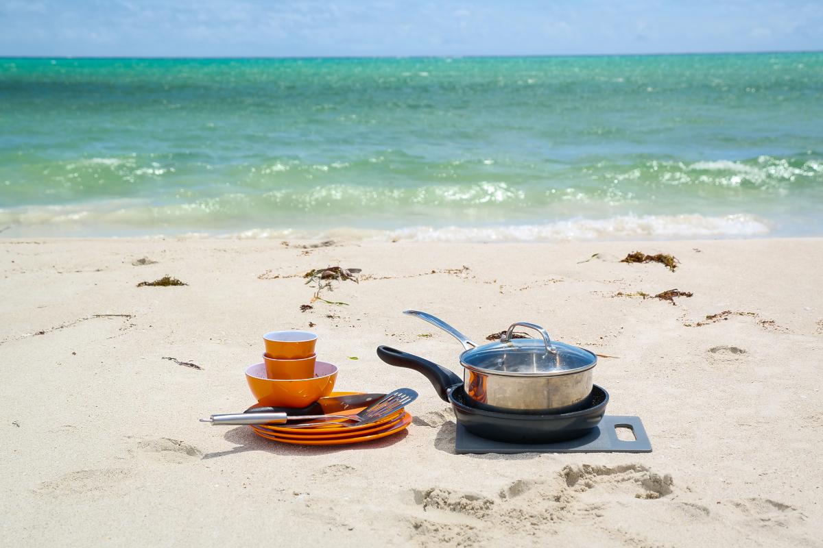 Pots, pans and plates sitting stacked on a white sand beach