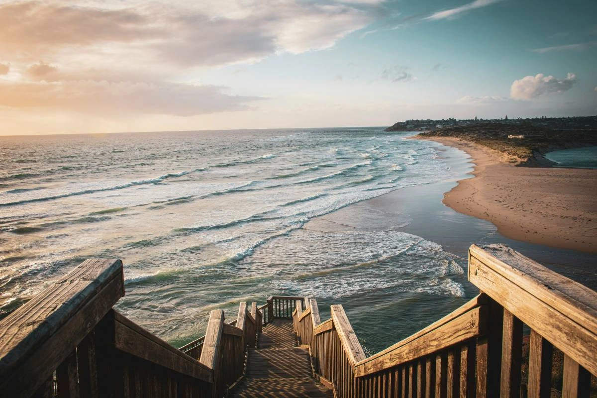 Wooden staircase leading down to a white sand beach with waves rolling in 