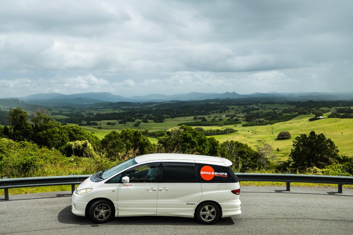 White campervan driving along a hill top road with green rolling landscapes below