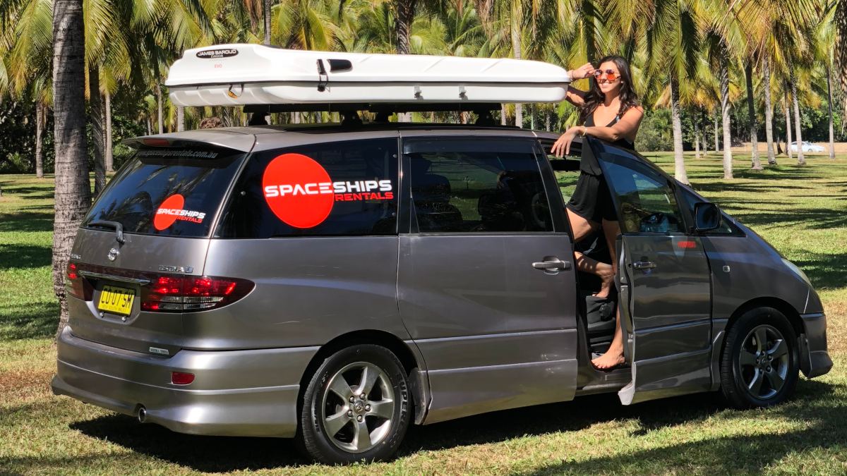 Campervan with a rooftop tent parked amoung palm trees with a women standing in the drivers seat door