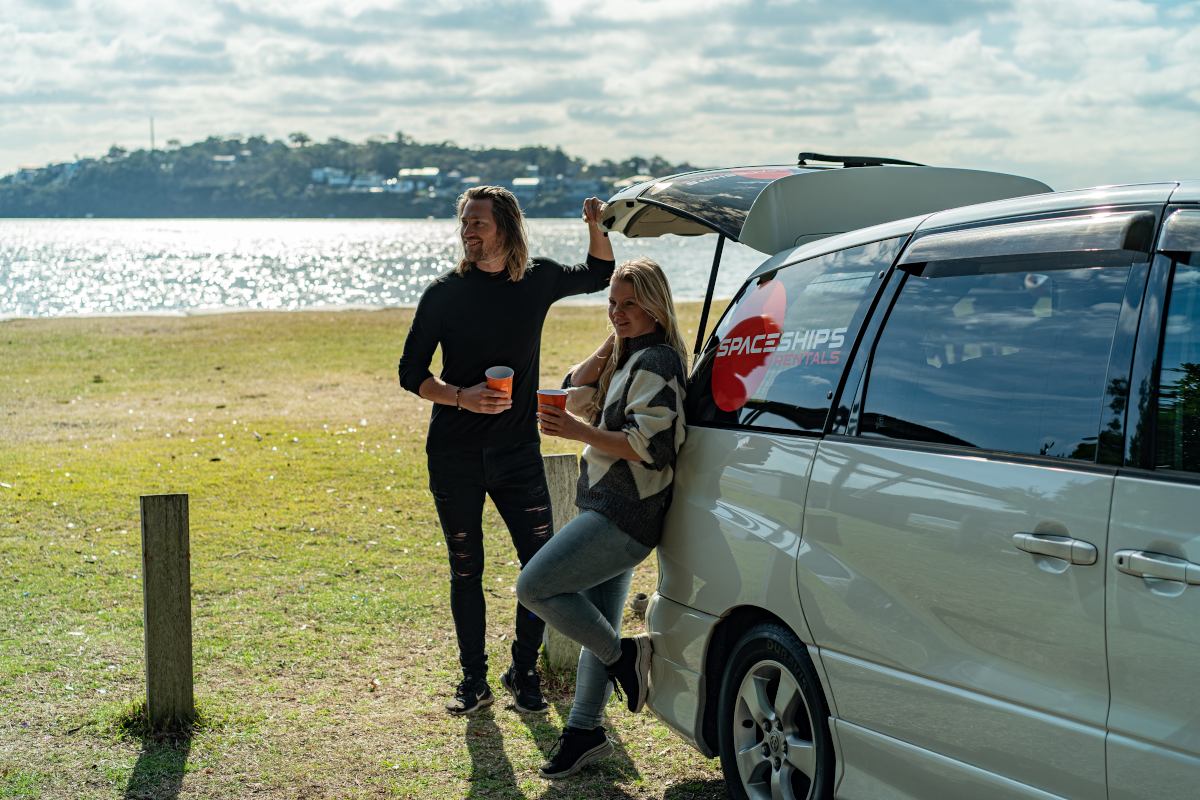 two people holding coffee cups standing outside their campervan