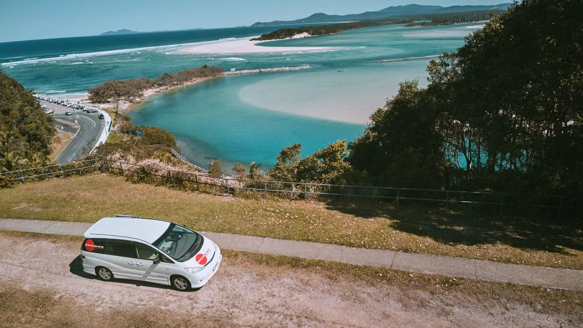 White campervan parked overlooking a harbour with swirling blue water and white sand