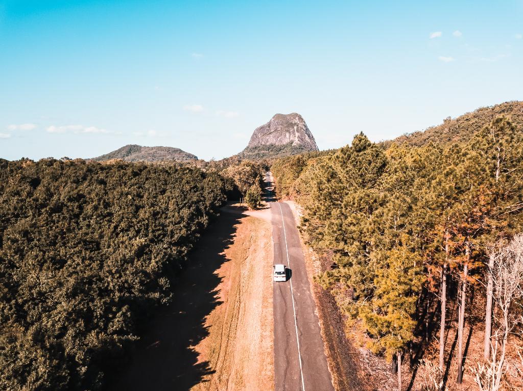 birds eye view of a camperva driving downa remote road in the forest towards a large rocky mountain