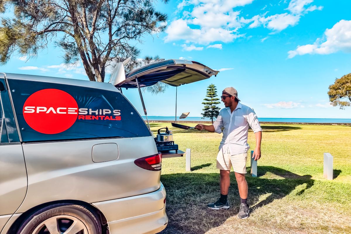 Man flipping bread in a pan cooking from the back of his campervan
