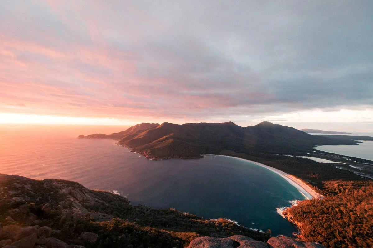view from a the top of a mountain looking down on a sweeping bay with white sand and blue water in Tasmania